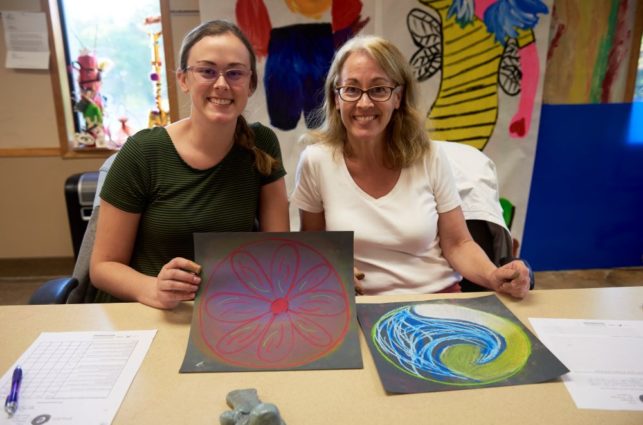 Two women smile for the camera and show off their artwork.