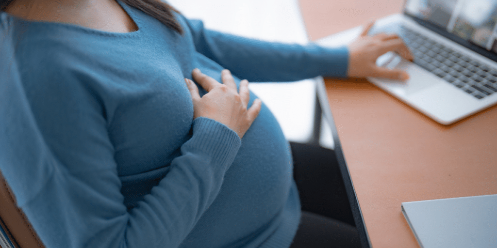 Pregnant person with hand resting on belly researching information on a laptop