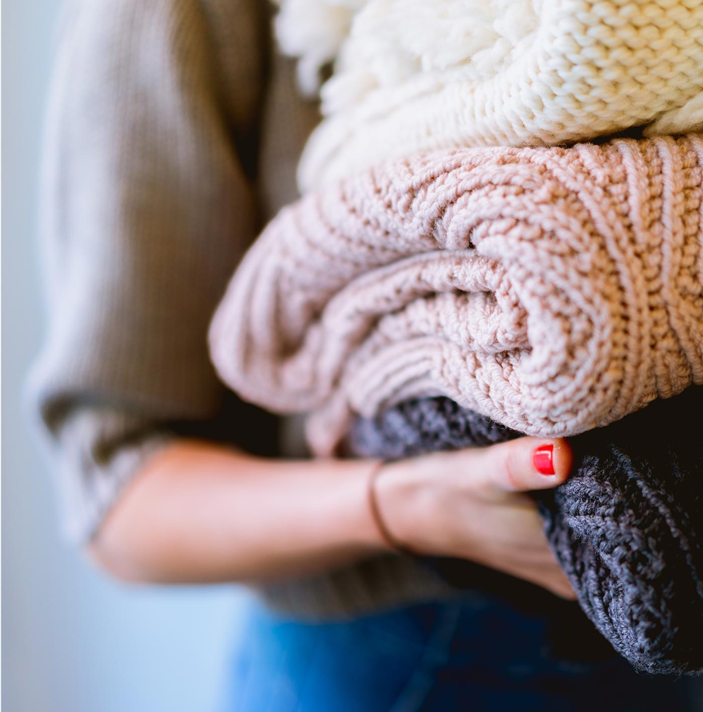 Close-up of a person holding a stack of folded knit sweaters.